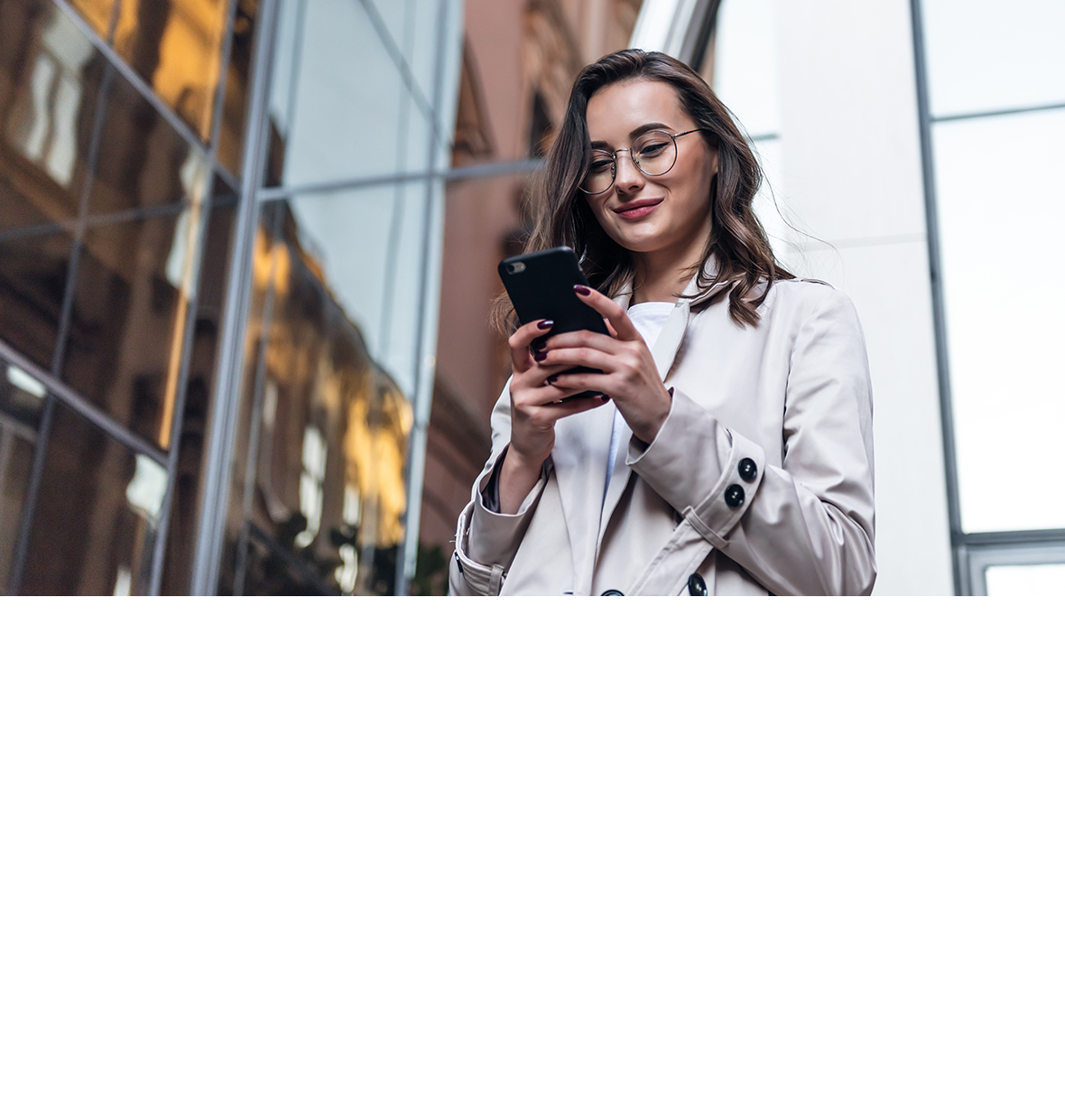 a young woman with thin framed glasses smiling and looking down at her phone